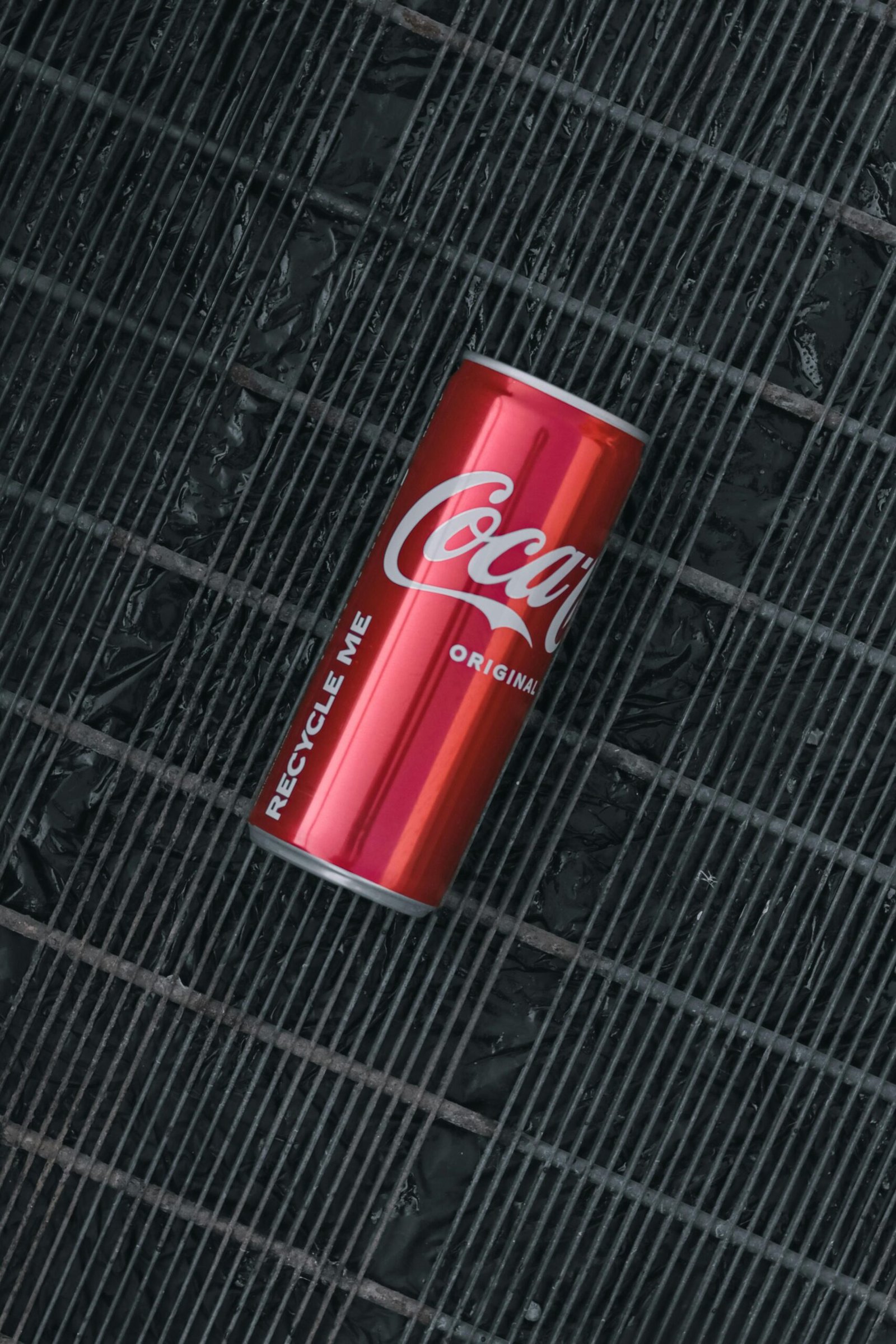 A vertical shot of a Coca-Cola can laying on a textured dark surface, emphasizing brand logo and recycle message.